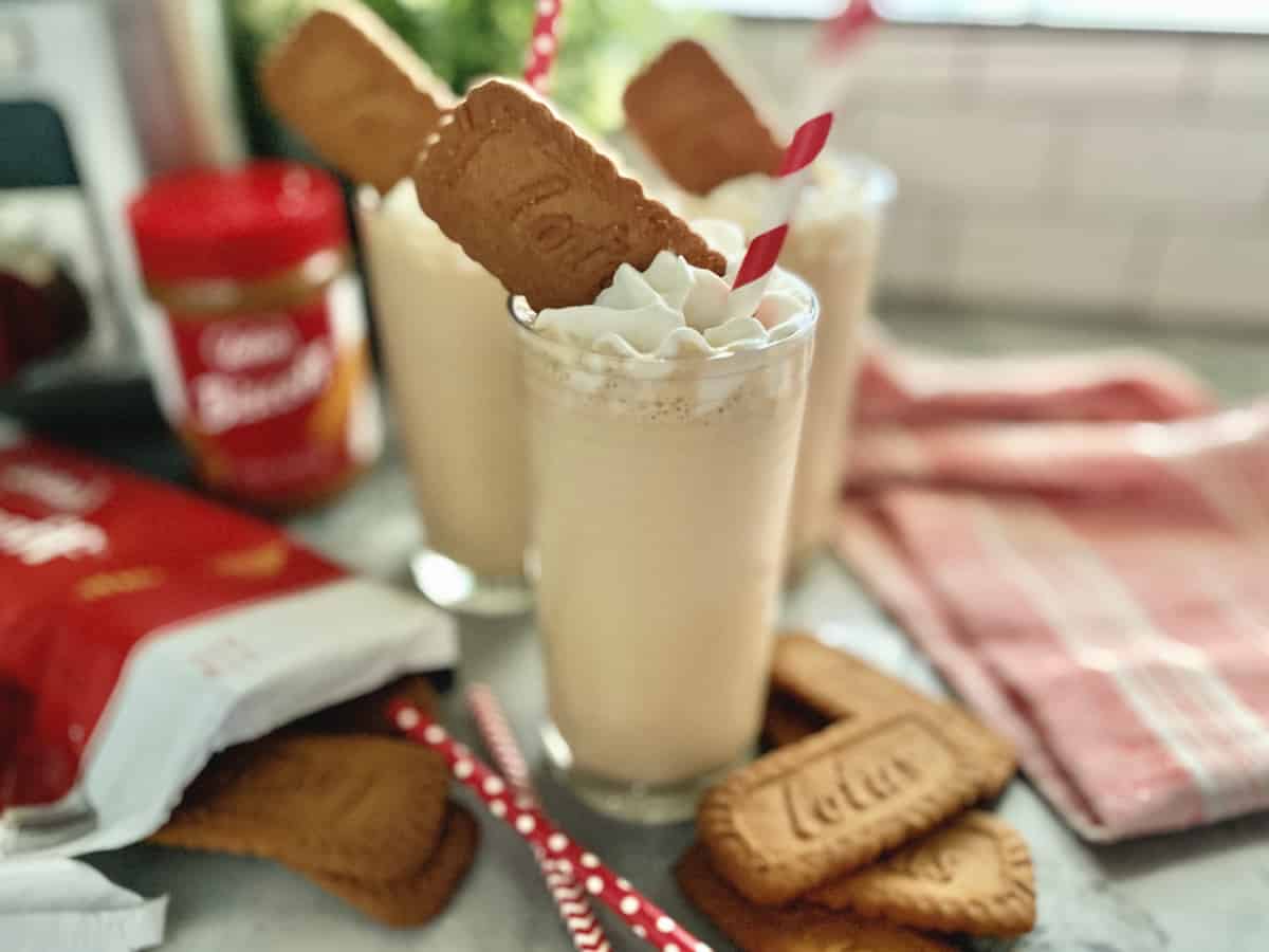 Three glasses bundled together with light brown milkshake, whipped cream, and cookies.