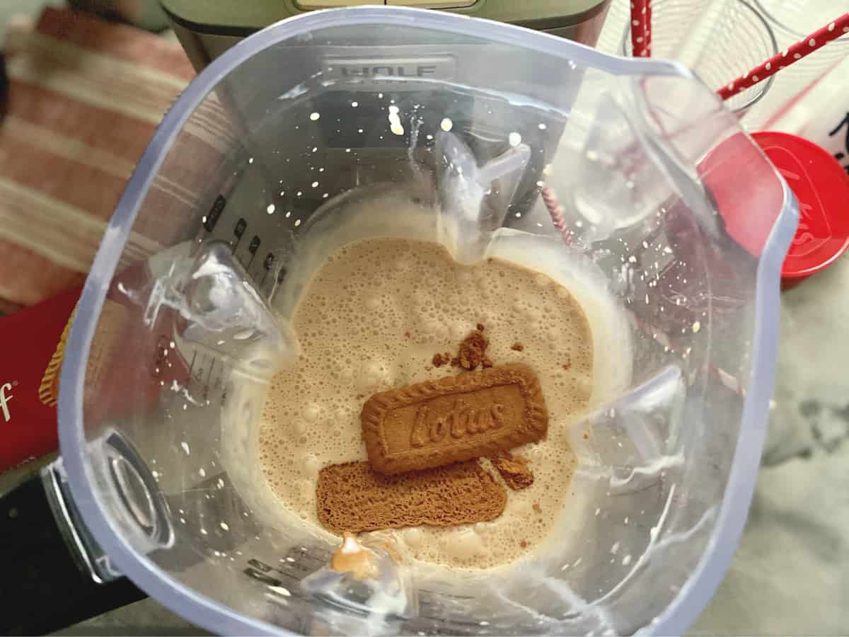 Top view of a blender pitcher with light brown blended liquid and lotus cookies.