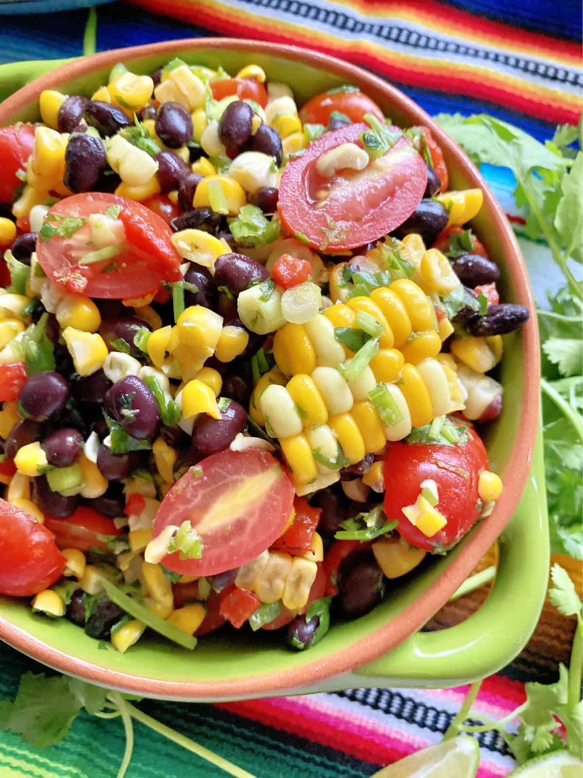 Top view of a green bowl filled with corn kernels, sliced grape tomatoes, cilantro, and black beans.