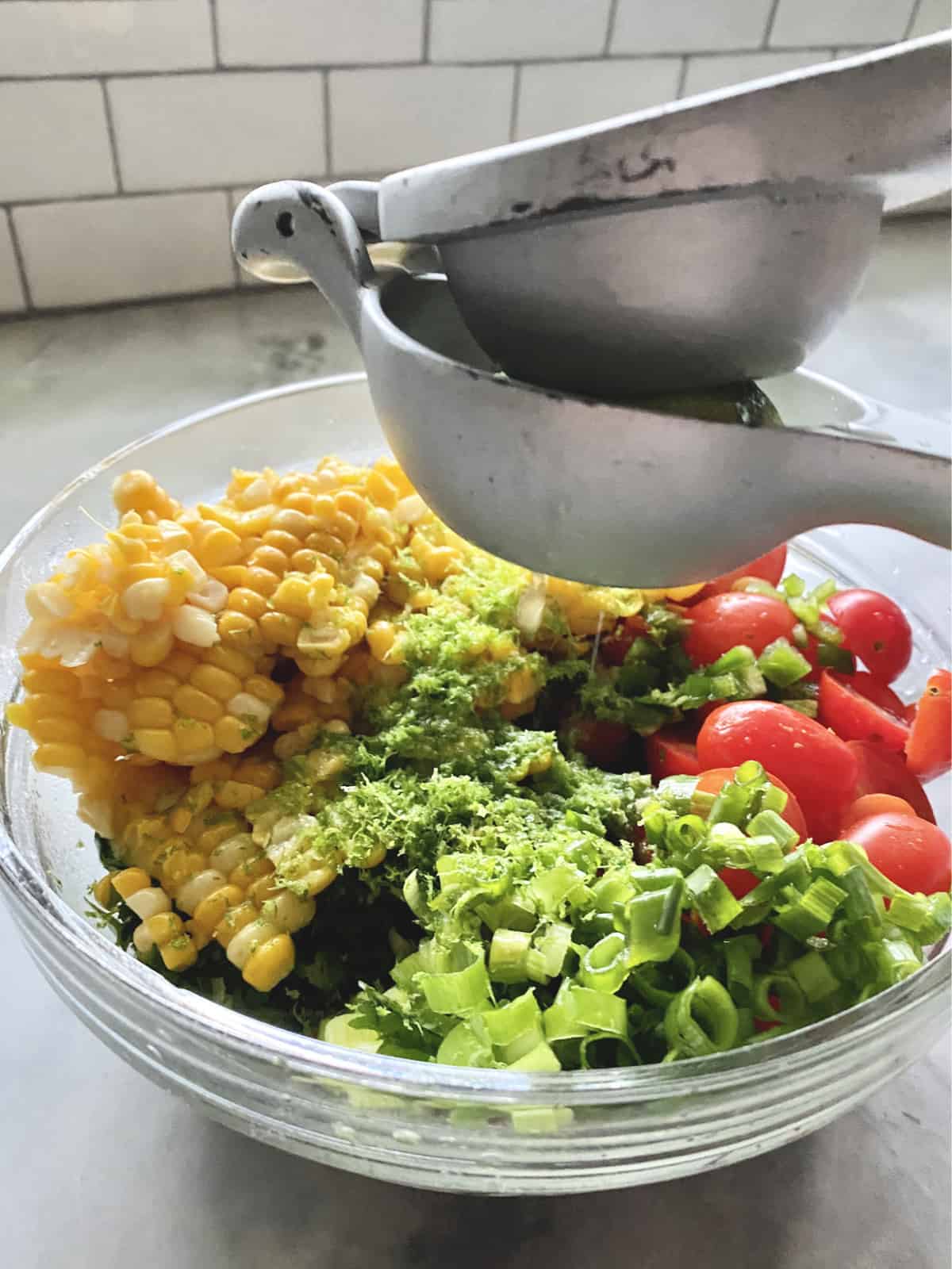 Juicer squeezing lime into a glass bowl with corn, tomatoes, green onions and lime zest. 