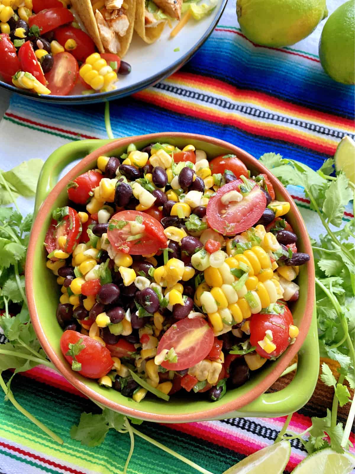 Top view of corn, black beans, and tomatoes in a green bowl with cilantro around it.