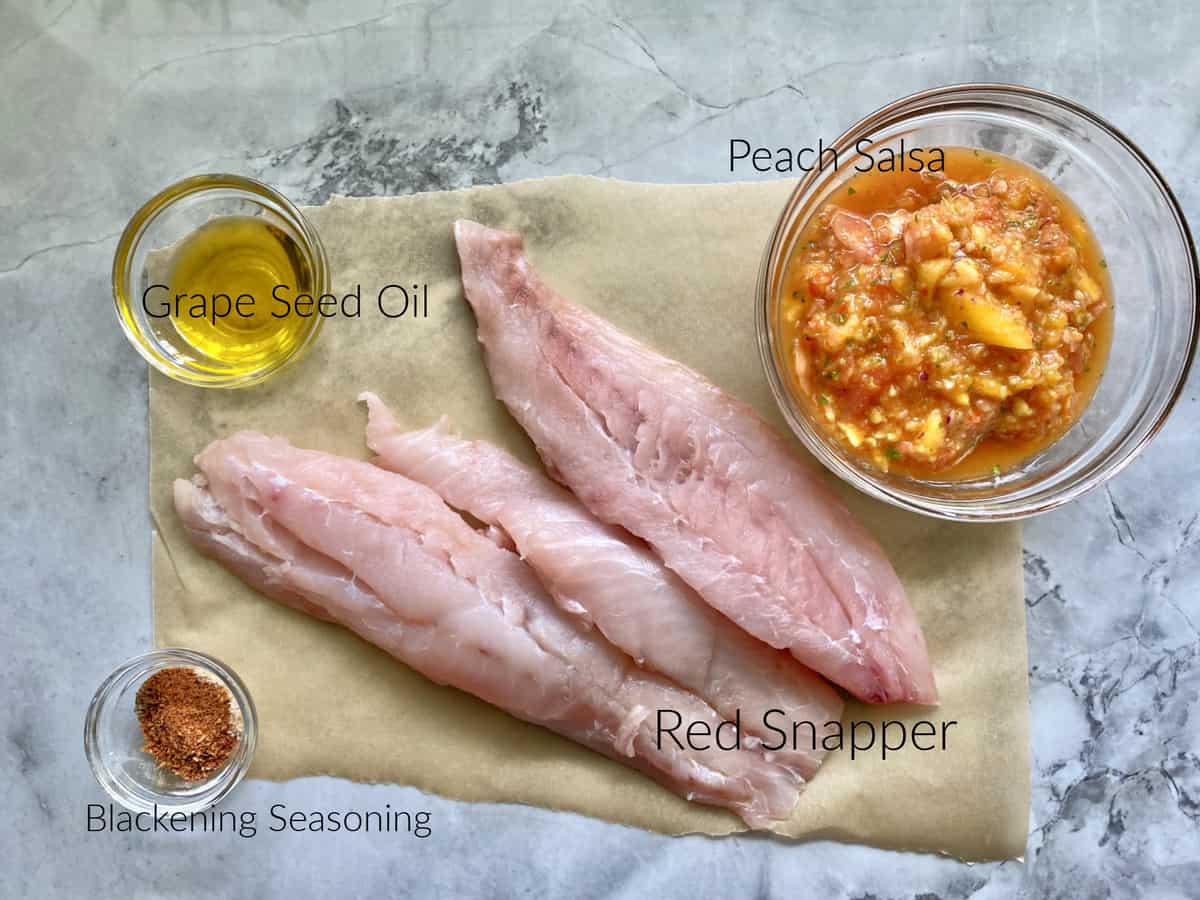 Ingredients on marble counter: grape seed oil, blackening season, red snapper, and peach salsa. 