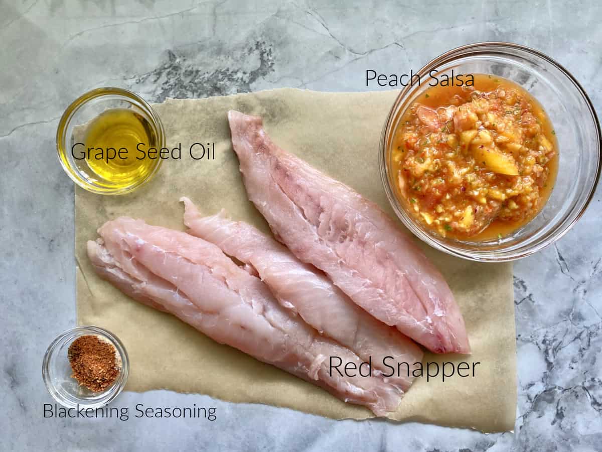 Ingredients on marble counter: grape seed oil, blackening season, red snapper, and peach salsa.