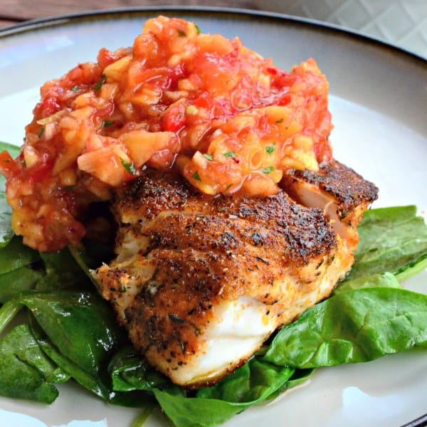 Blackened snapper with peach salsa on top all resting on a bed of spinach.