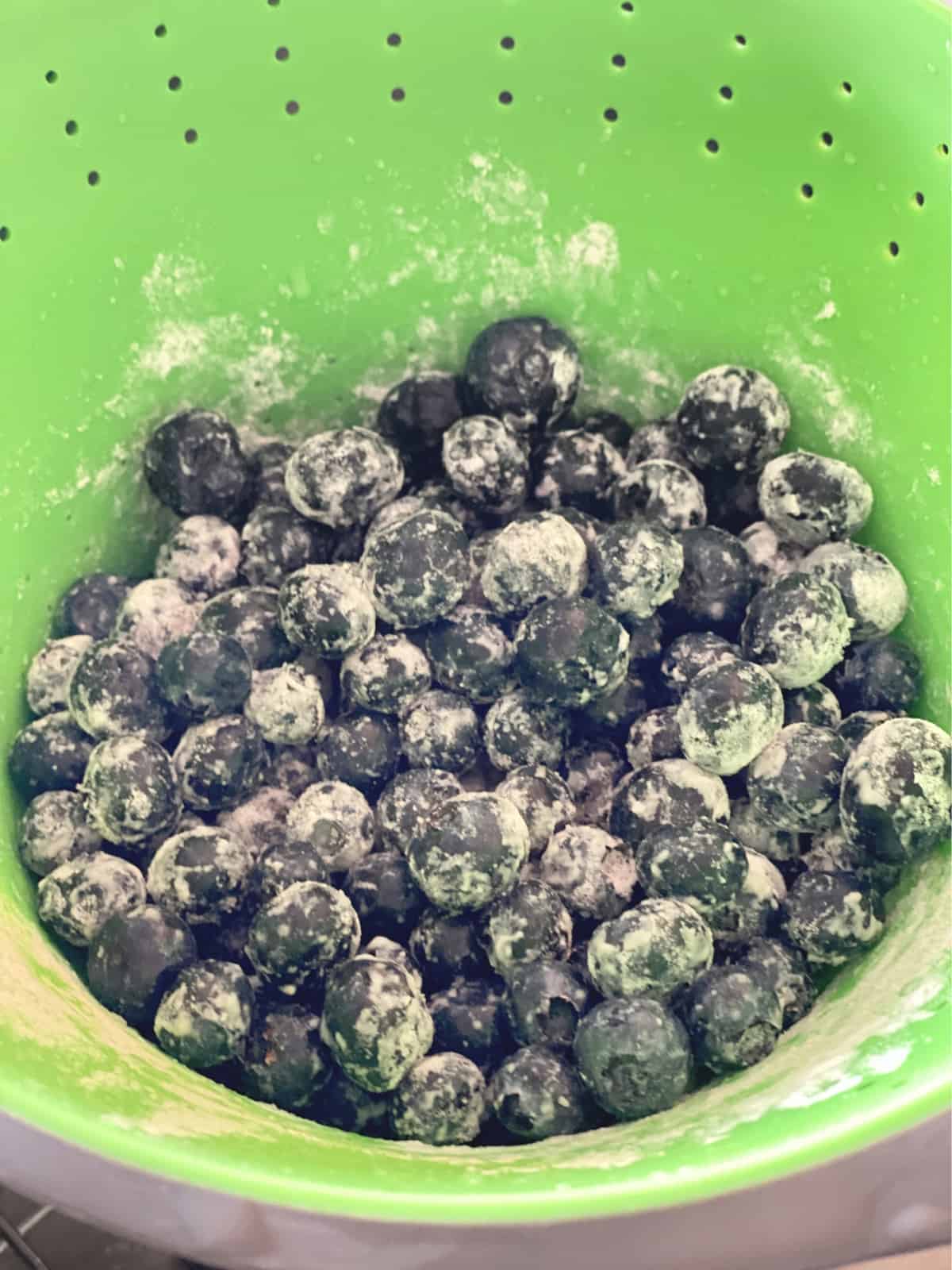 Floured blueberries in a neon green colander. 