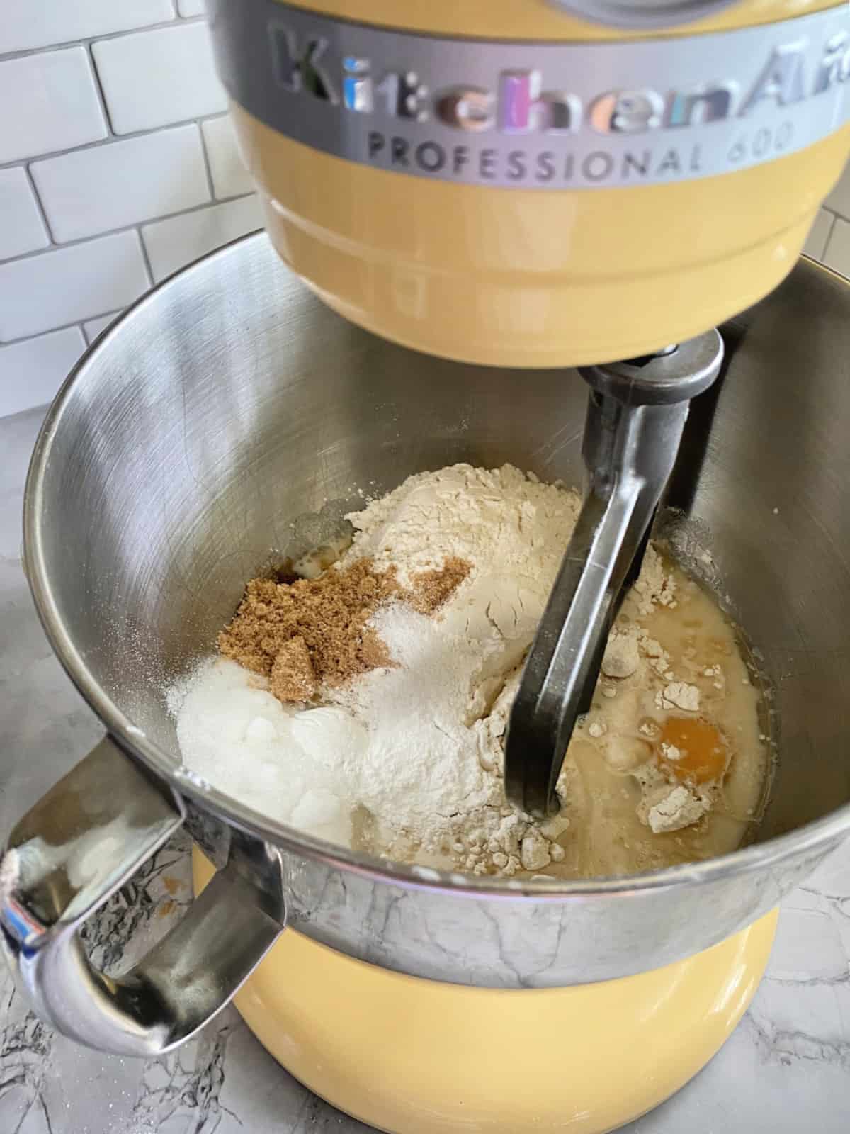 Dry and wet ingredients in a stainless steel mixing bowl attached to a KitchenAid Yellow Mixer.