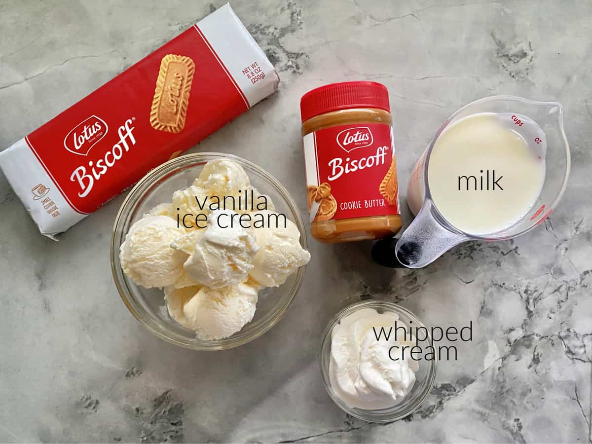 Ingredients on marble countertop, Biscoff cookies, spread, milk, whipped cream, and ice cream.