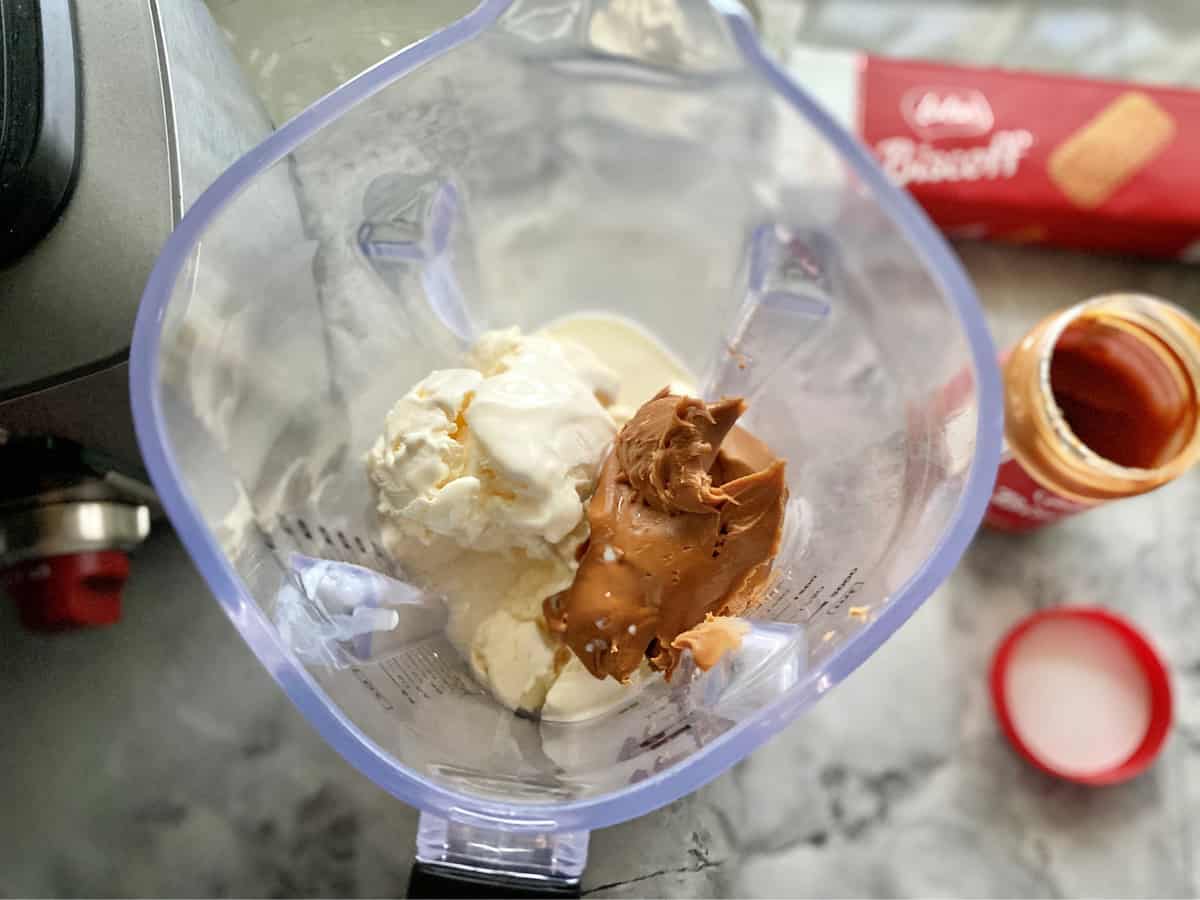 Top view of a blender on a marble counter filled with vanilla ice cream and biscoff cookie spread.