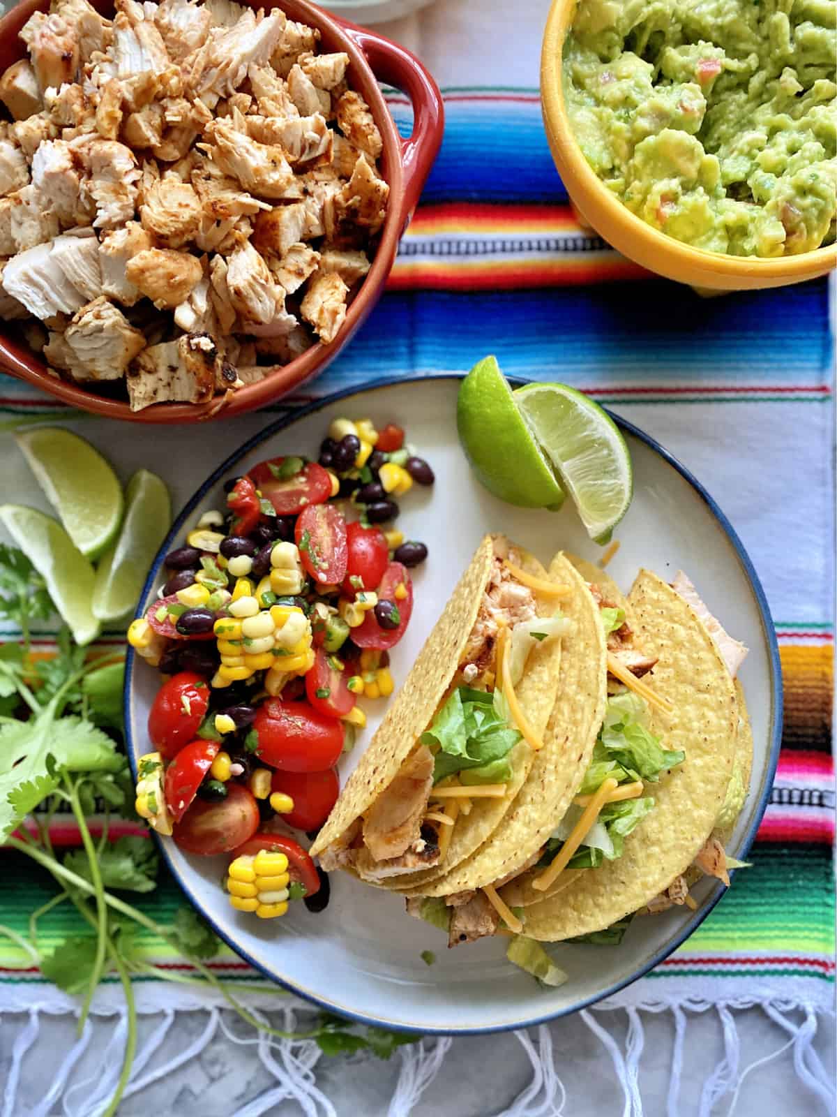 Top view of three chicken hard shell tacos with black bean salad on a plate with limes. 