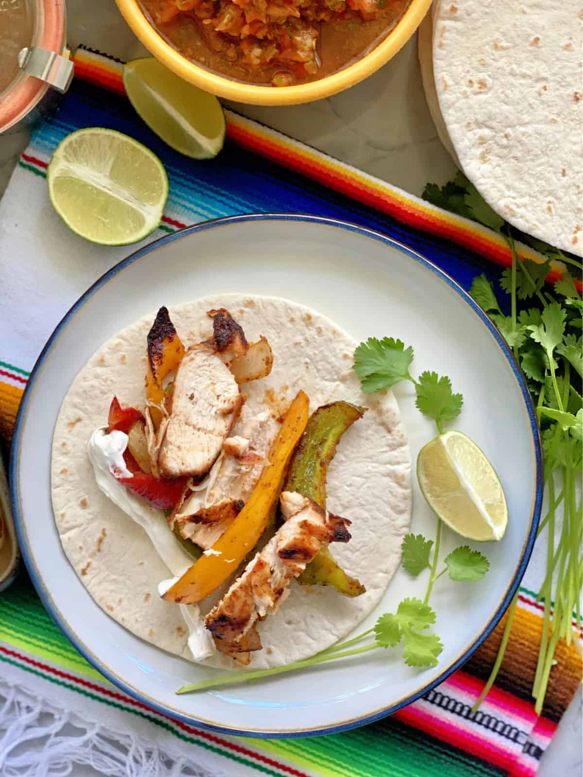 Top view of a flour tortilla on a white plate filled with grilled chicken, peppers, and sour cream.