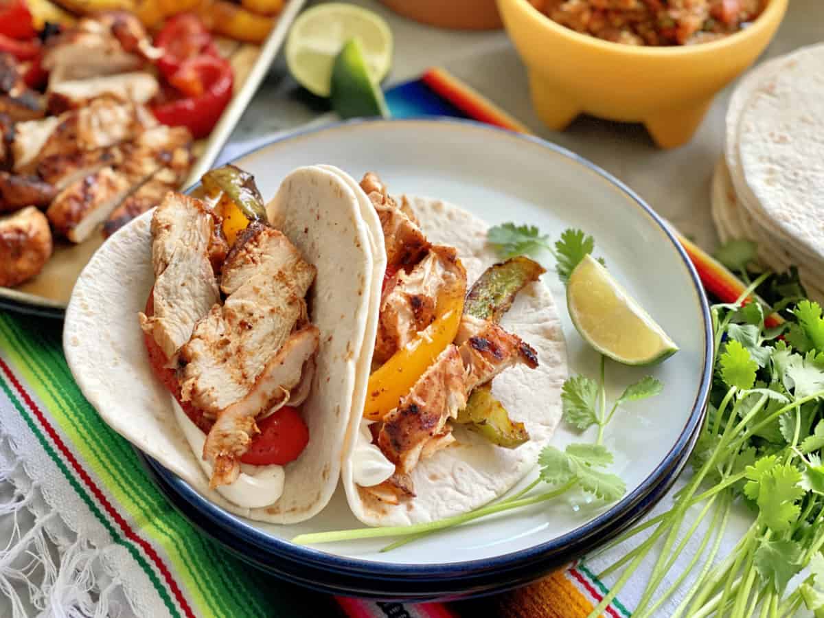 Two flour tortillas folded on a white plate filled with grilled chicken, fajitas, and sour cream.