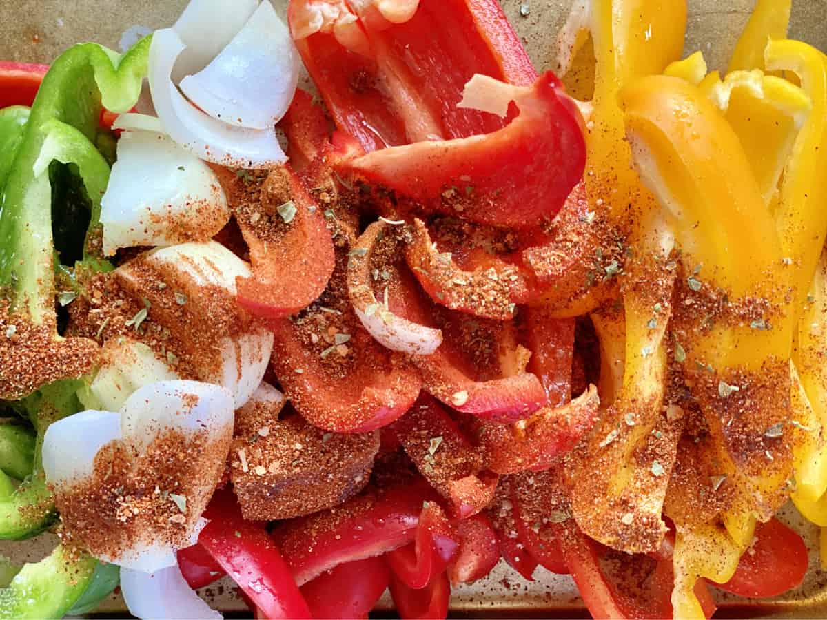 Top view of cut bell peppers and onions with seasoning sprinkled on top. 