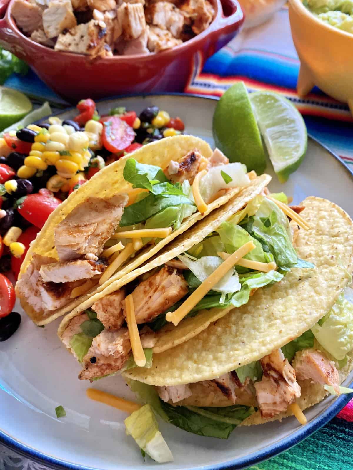 Three hard shell tacos stuffed with chopped chicken, lettuce, cheese on a white plate.