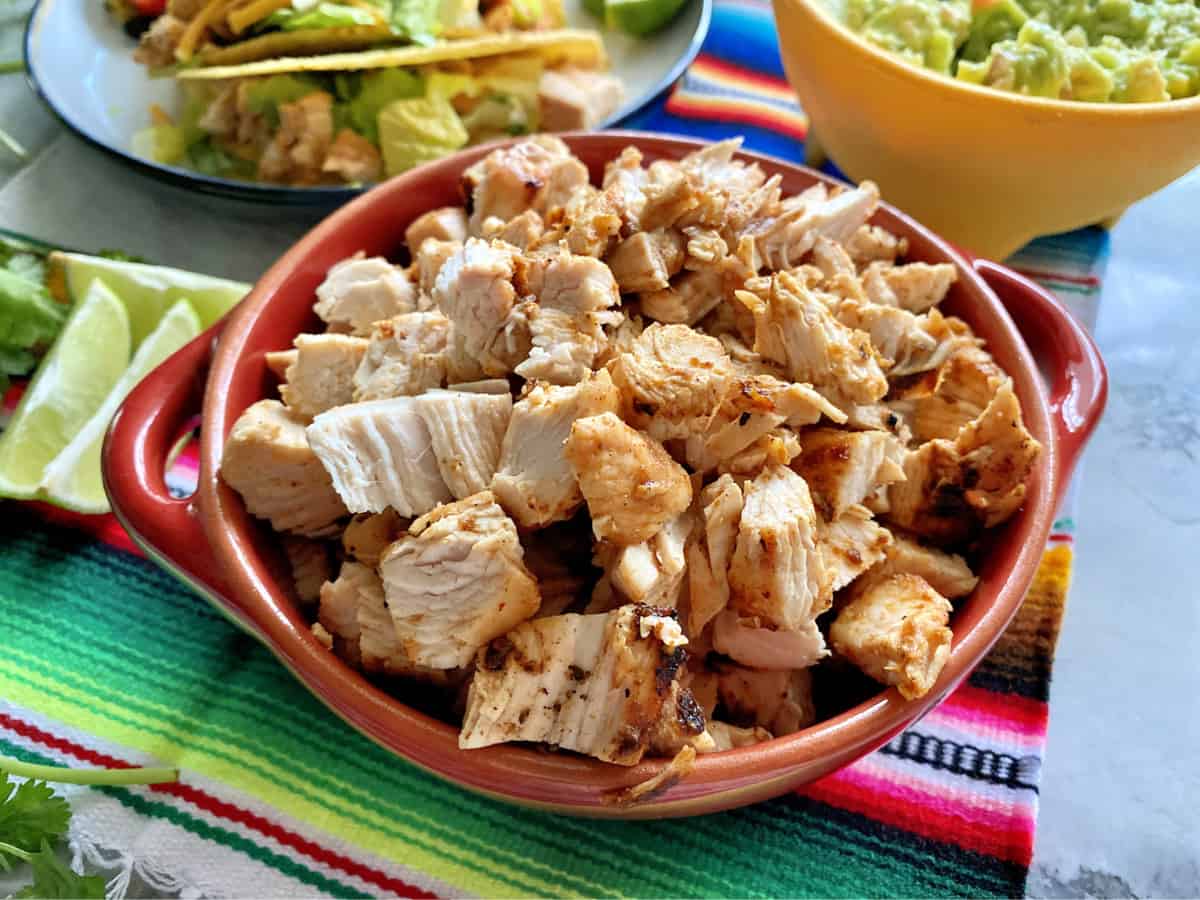 Chopped grilled chicken in a red bowl with limes and taco in the background.