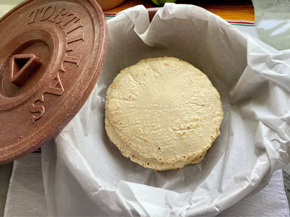 Stack of tortillas sitting on white parchment paper in a tortilla warmer. 