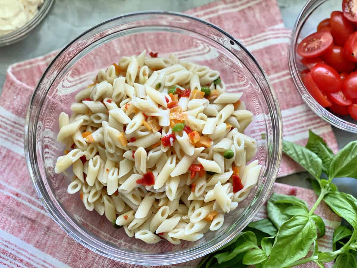 Top view of cooked pasta with vegetables in a clear glass bowl on a red and white cloth.