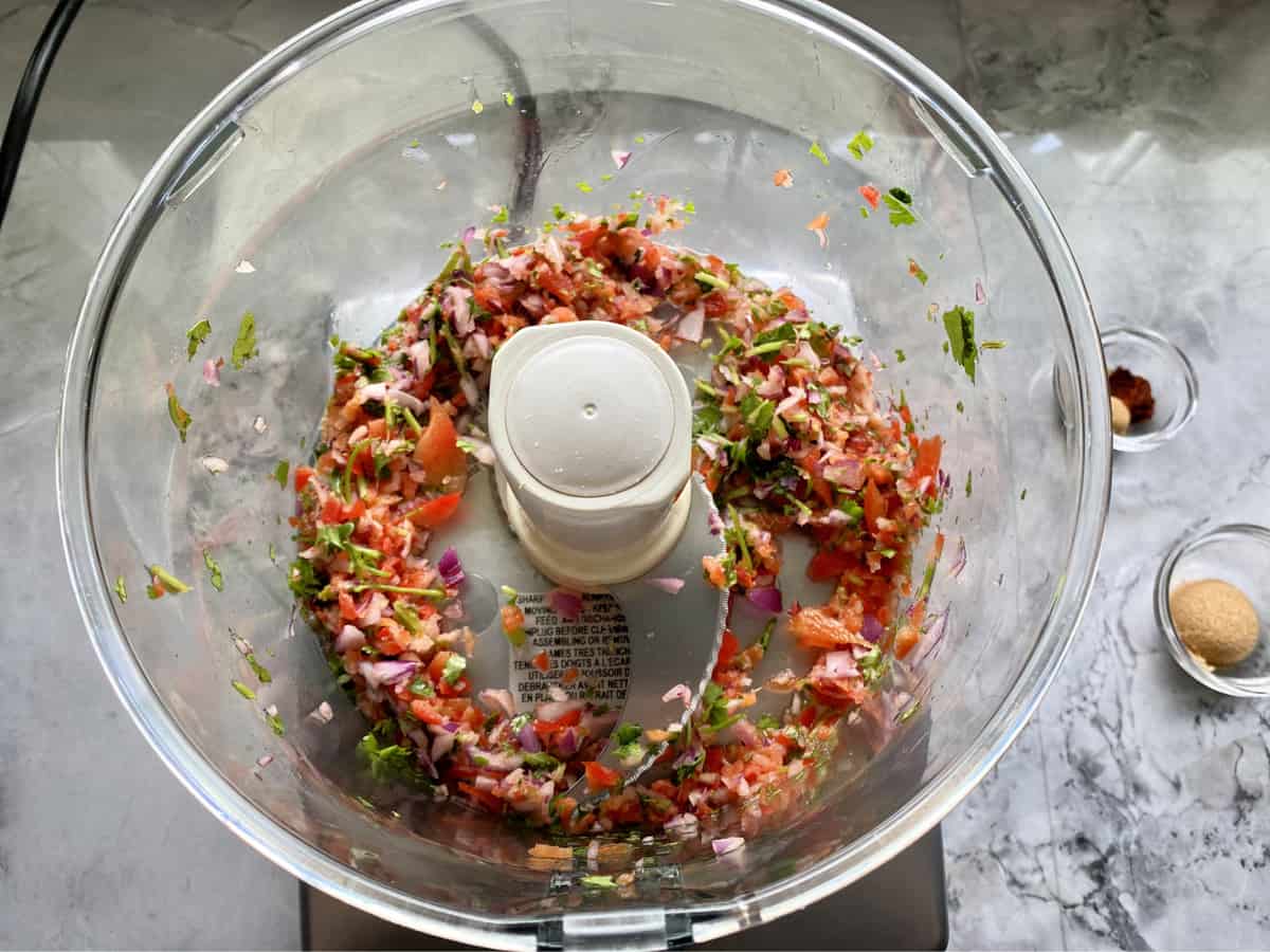 Top view of food processor with chopped red onion, cilantro, and red bell pepper.