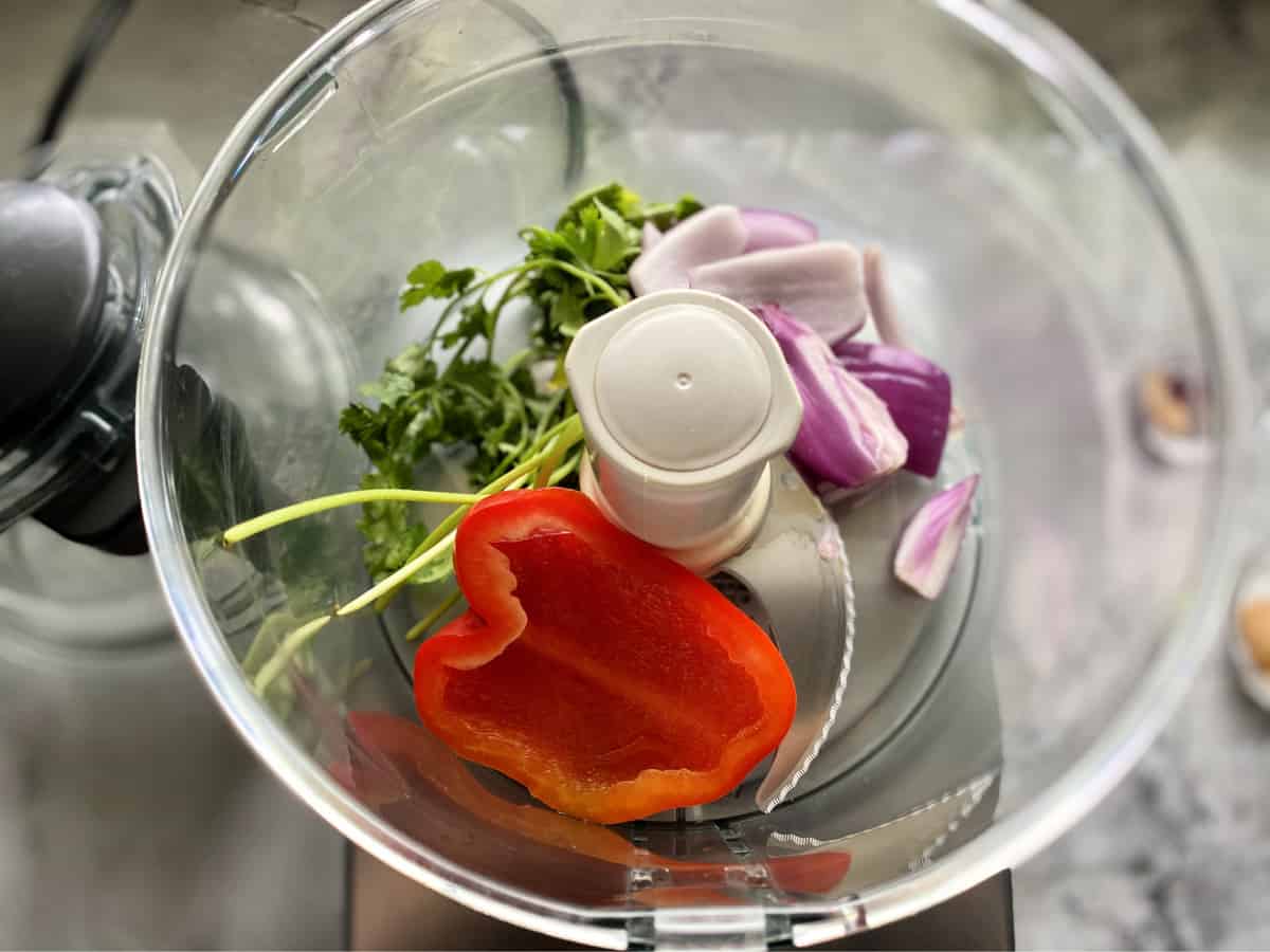 Top view of food processor with red bell pepper, red onion, and cilantro.