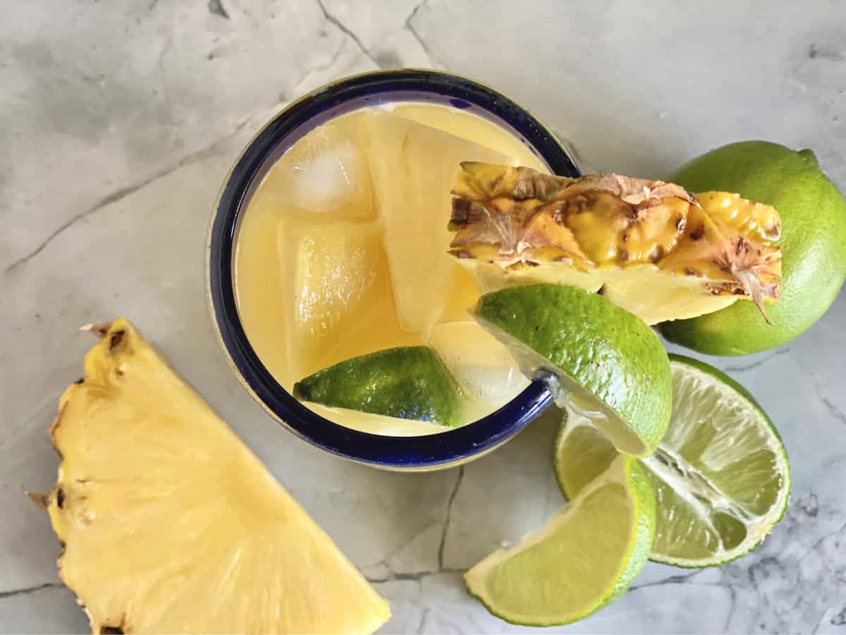 Top view of a glass filled with pineapple tequila drink with lime wedges and pineapple.