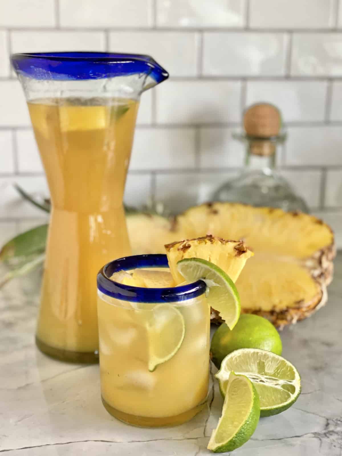 Pitcher of pineapple cocktail in the background with a glass in the foreground.