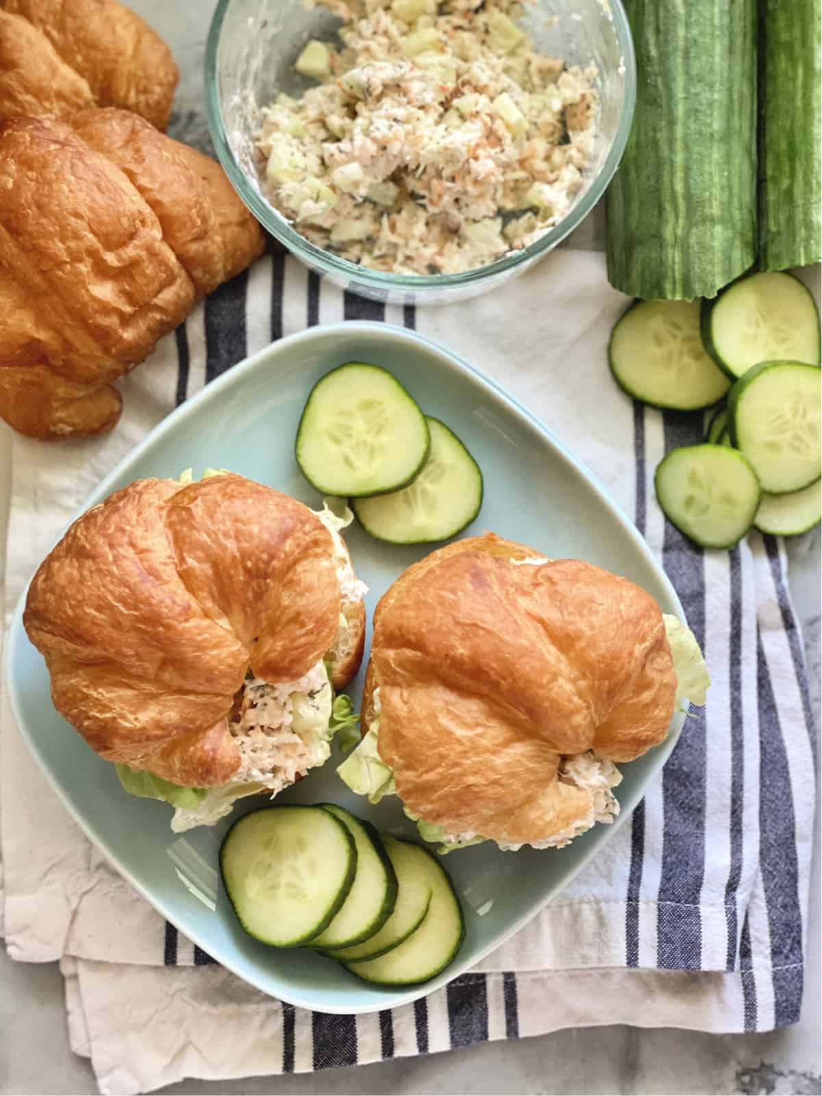 Top view of a square blue plate with croissants filled with shrimp salad and cucumber slices.