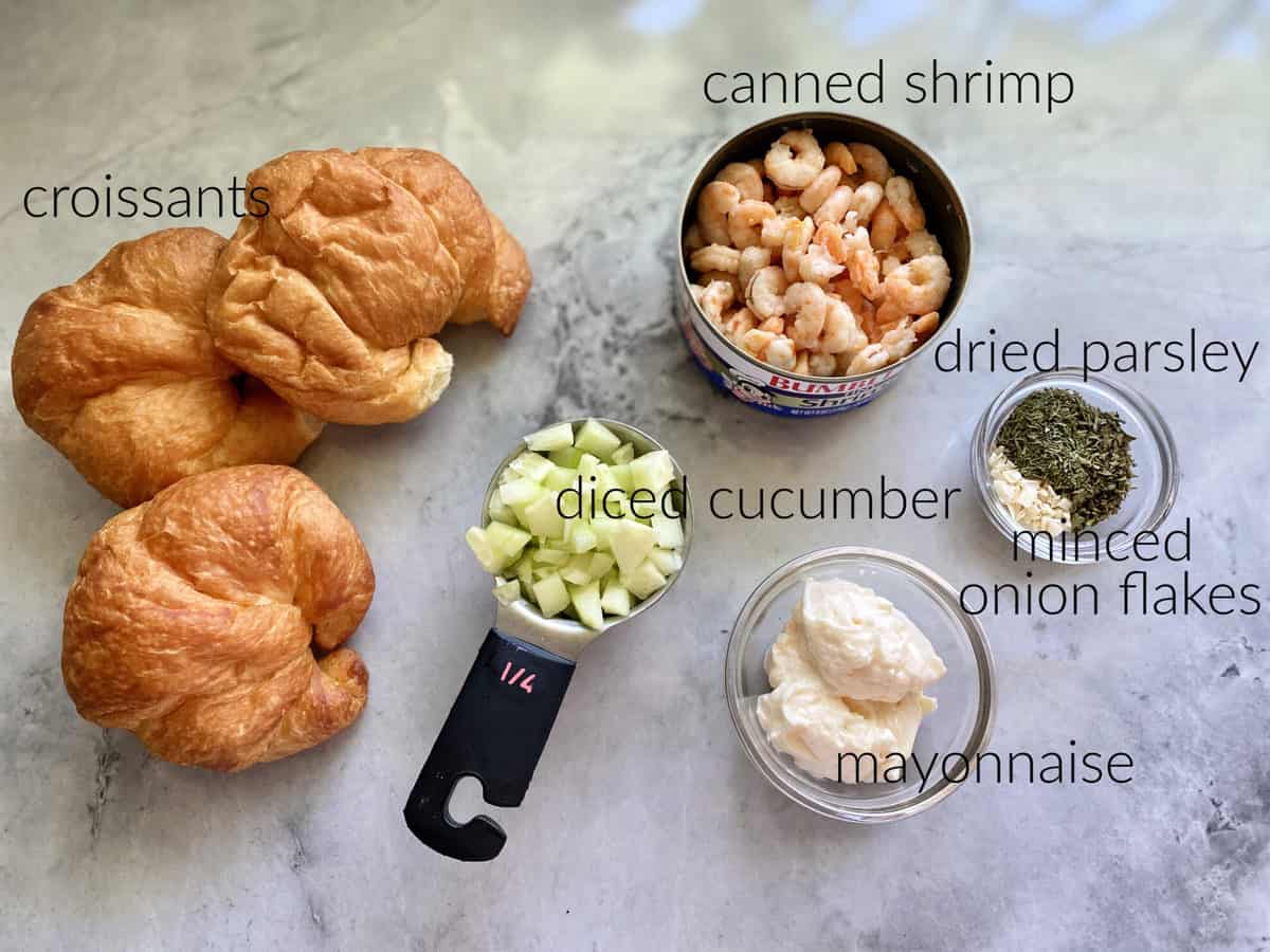 Ingredients on marble countertop: croissants, cucumber, shrimp, parsley, onion, & mayonnaise.