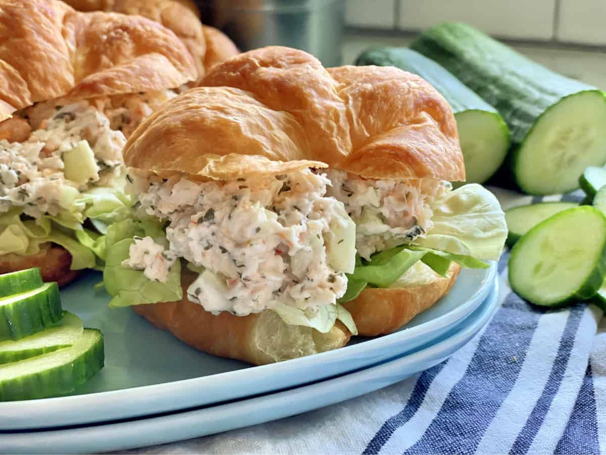 Two blue square plates with two croissants filled with shrimp salad and lettuce.