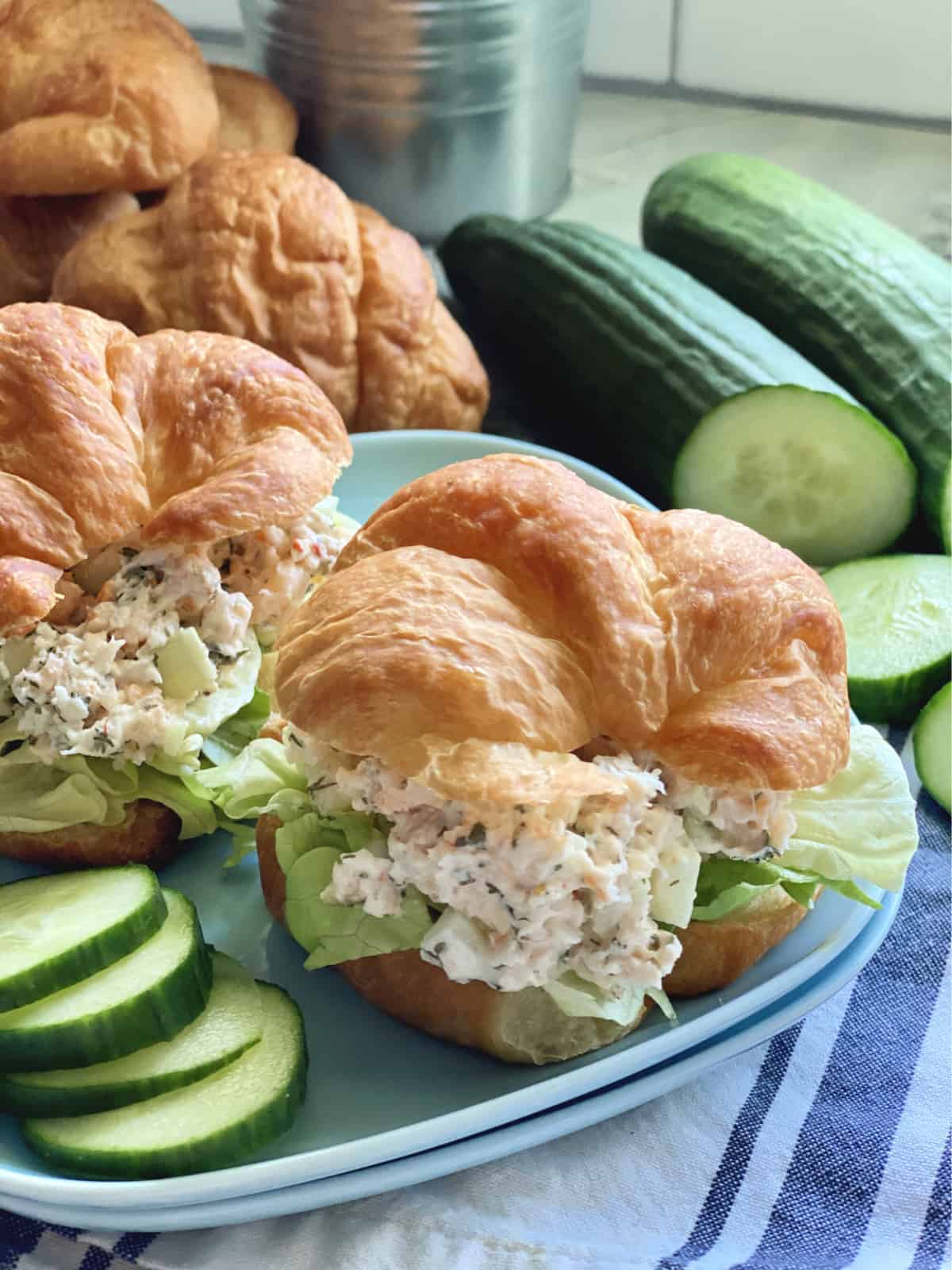 Blue plate with two croissants filled with a creamy salad and lettuce with cucumber slices on the side.