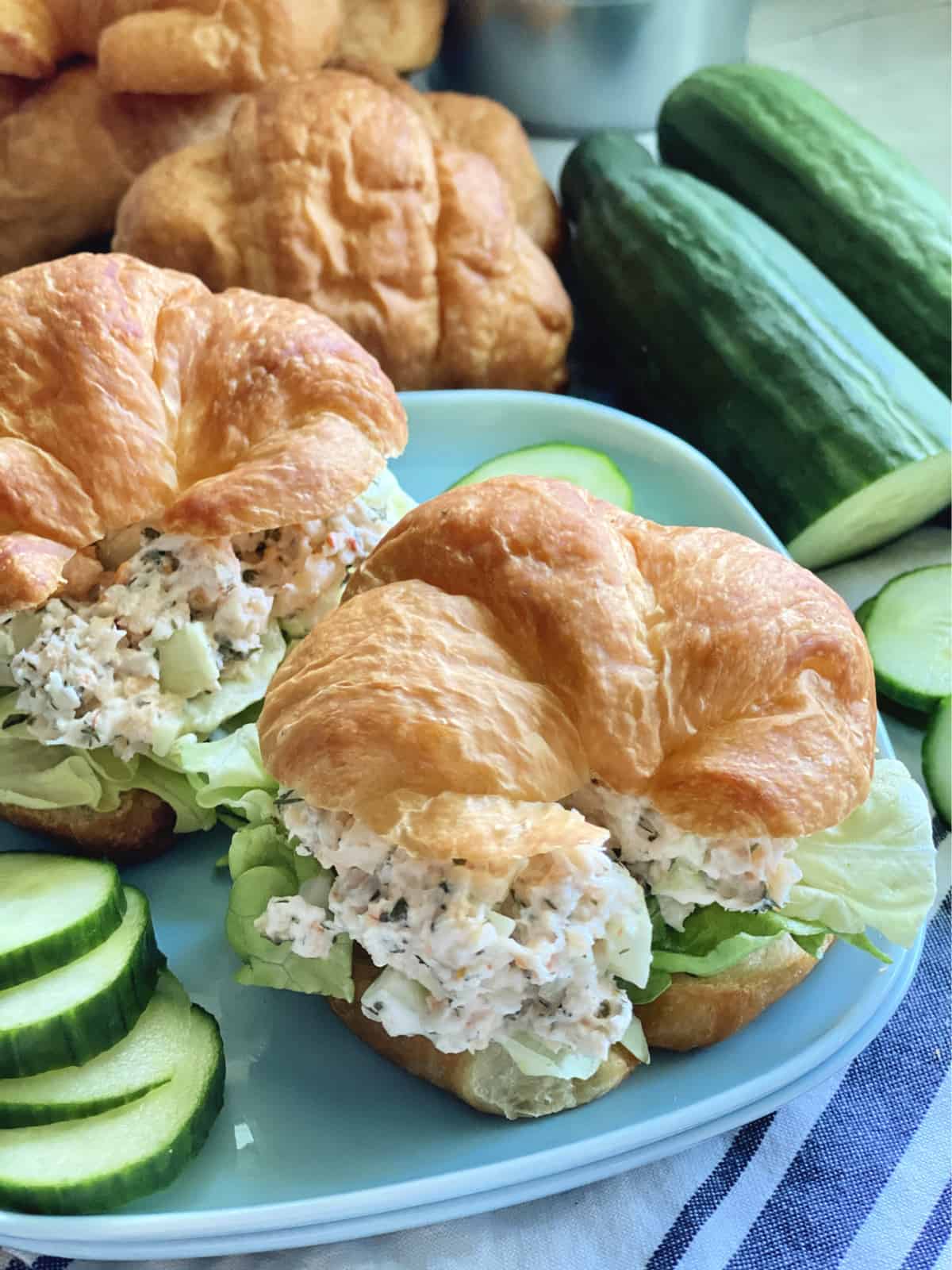 Close up of two croissants filled with seafood salad and lettuce with cucumbers on the side.