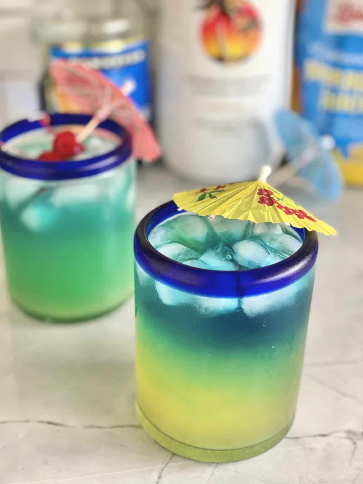 Two blue drinks with paper umbrellas and cherries in the drink.