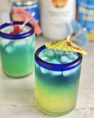 Two yellow blue drinks with paper umbrellas in glass.