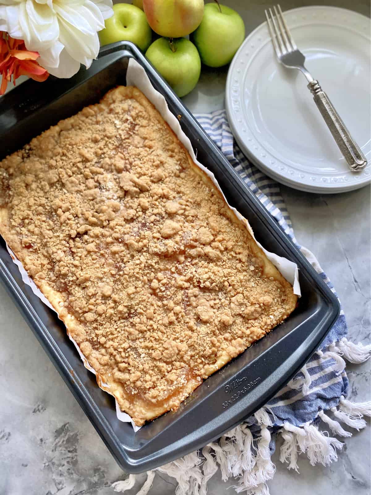 Top view of a pan of cheesecake bars with a streusel topping in a metal pan with parchment paper.
