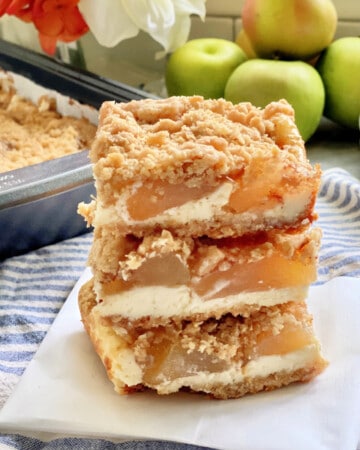 Three cheesecake bars with apples stacked on a piece of white partchment paper.