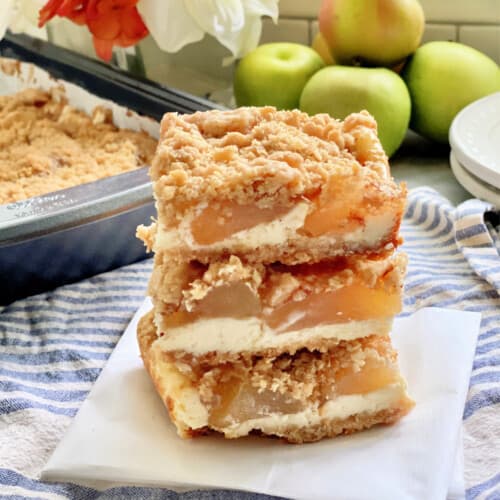 Three cheesecake bars with apples stacked on a piece of white partchment paper.