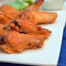 Baked spicy orange buffalo wings and drums on a white platter.