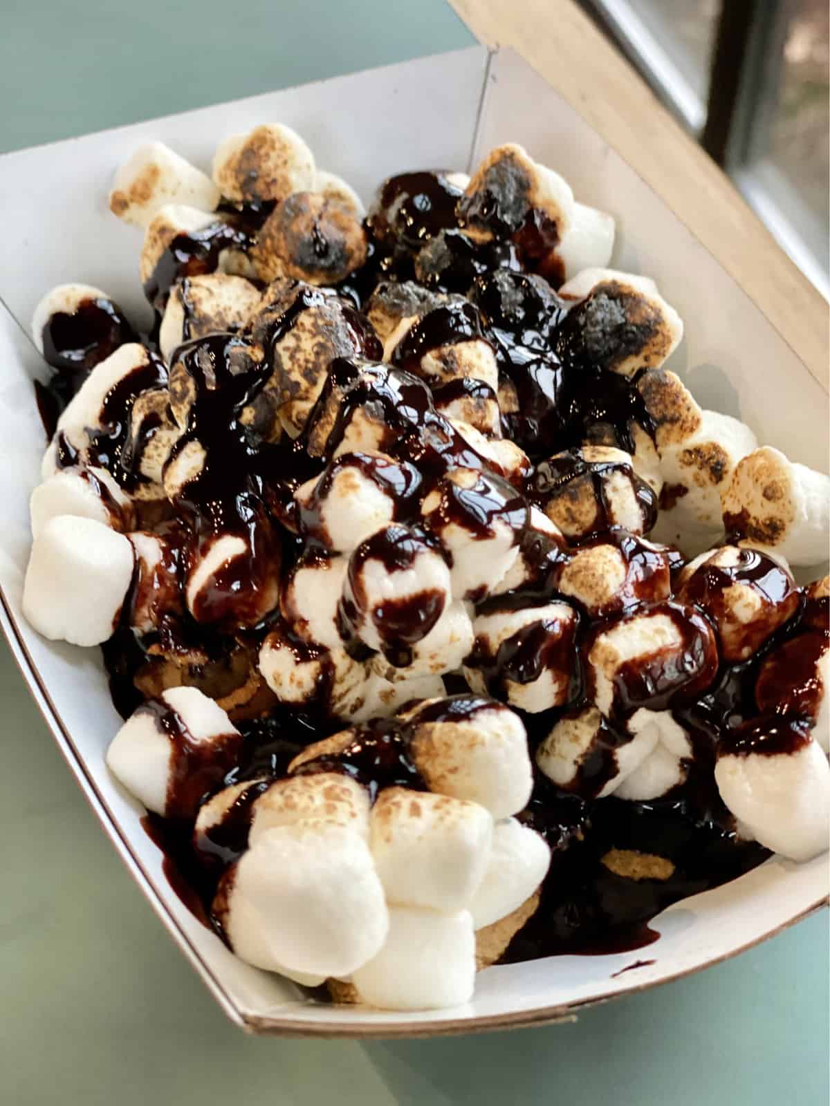 Paper tray full of marshmallows with chocolate sauce drizzled on top.