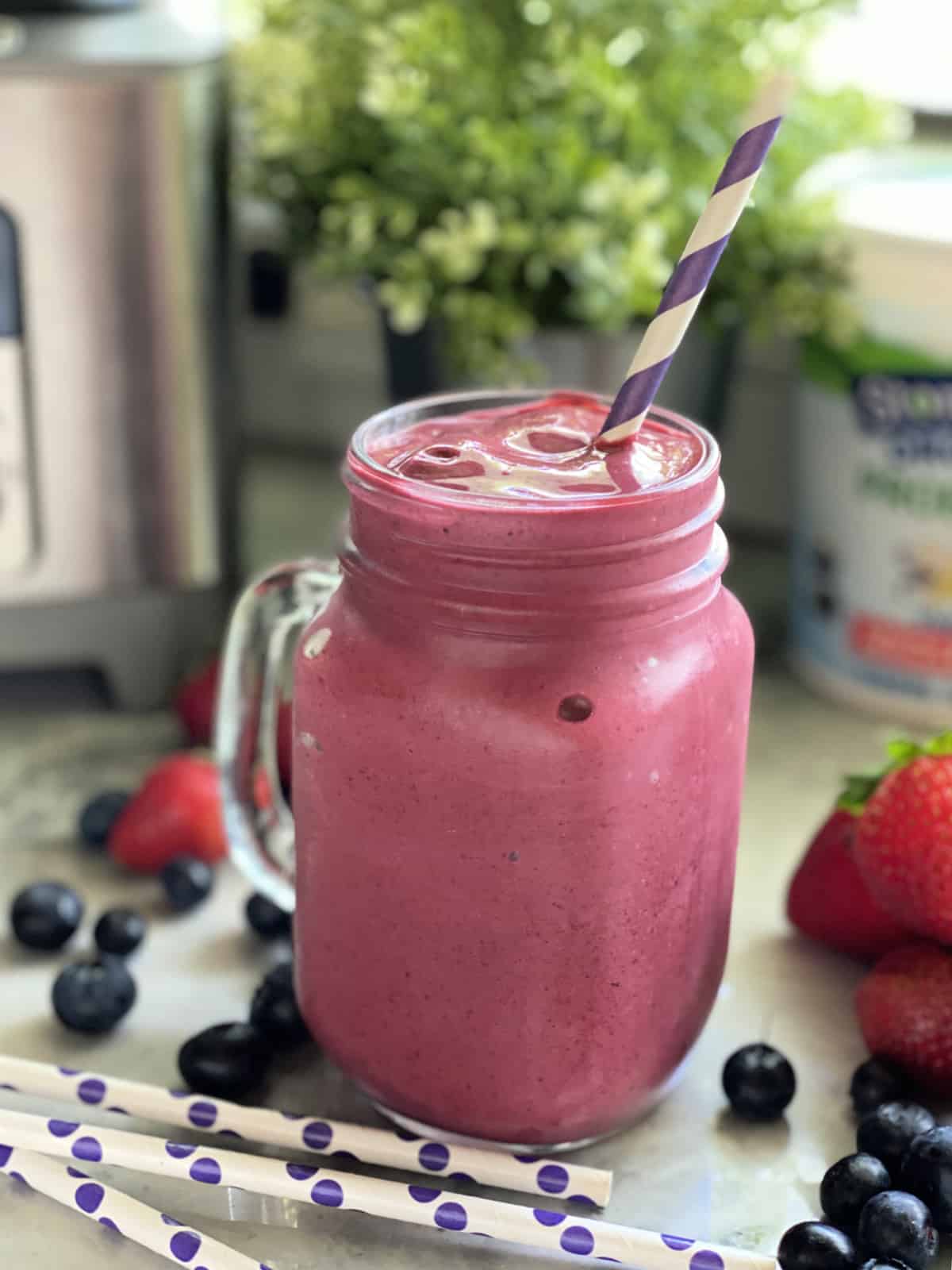 Mason jar glass with handle filled with purple smoothie with purple and white stripped straw. 