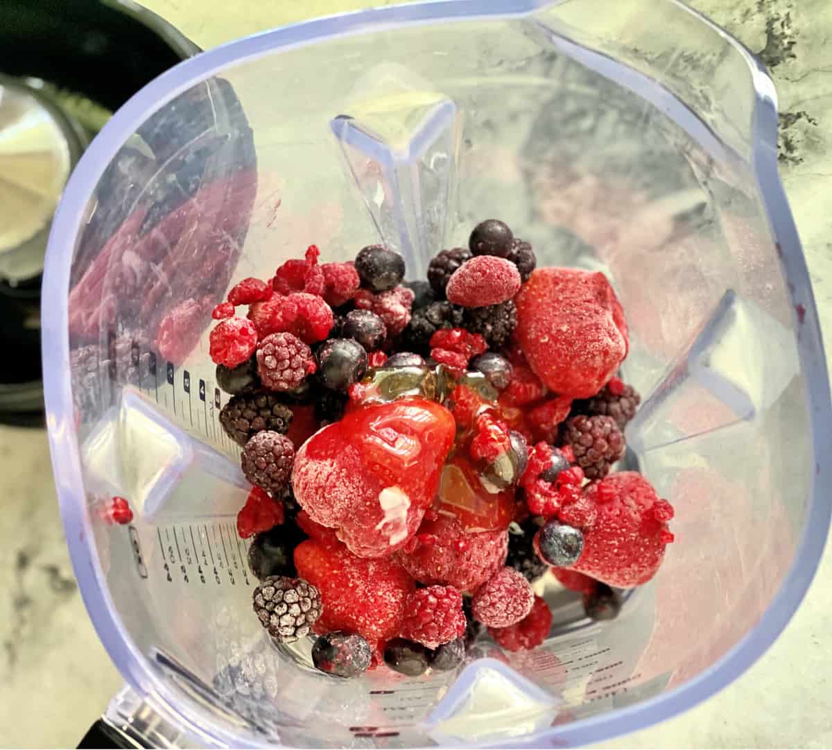 Top view of an open blender filled with frozen berries and honey.