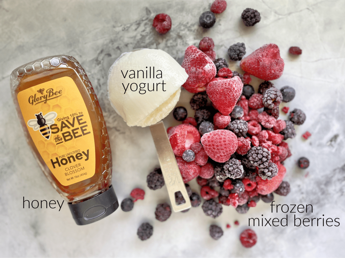 Ingredients on marble countertop: frozen mixed berries, vanilla yogurt, and honey.