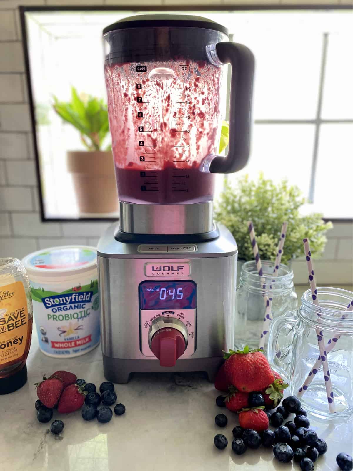 Wolf gourmet blender with purple smoothie in blender, clear glasses and ingredients next to blender.