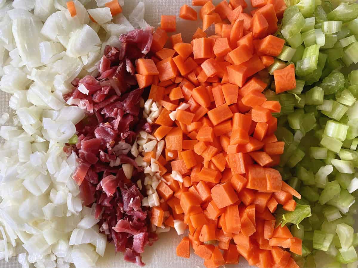 Diced onions, pancetta, carrots and celery on white cutting board.