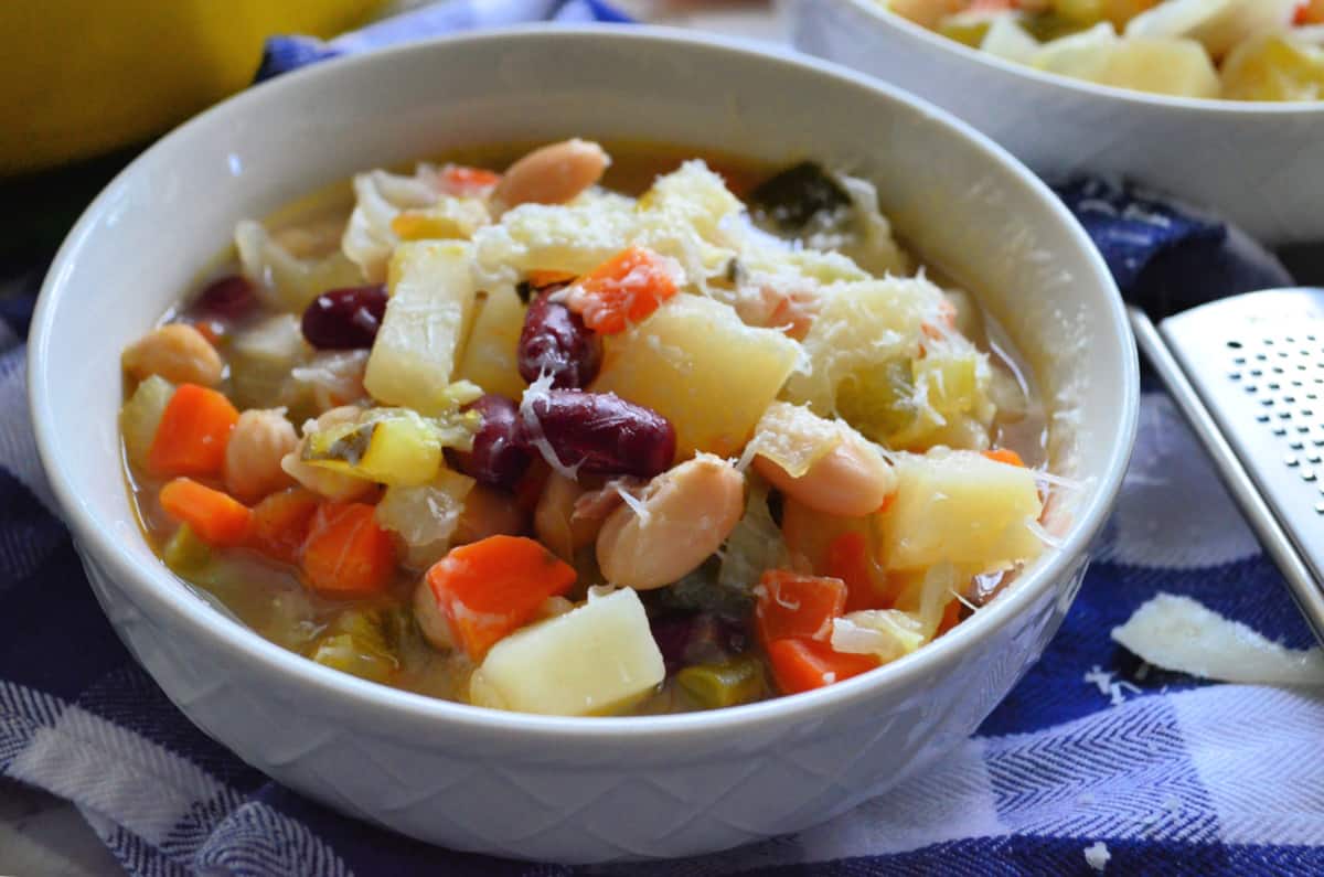 Two white bowls filled with minestrone soup topped with shredded parmesean cheese.