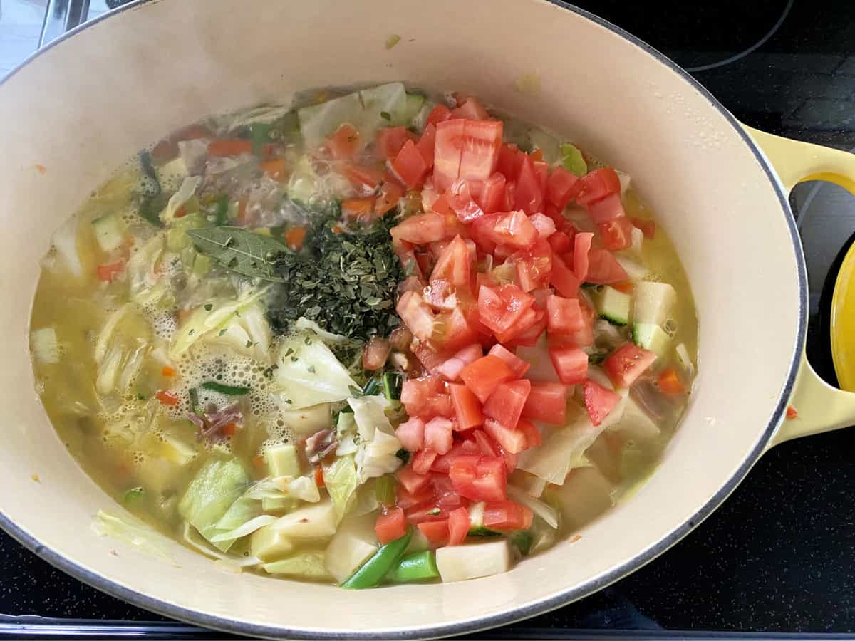 Top view of fresh tomatoes, spices, and vegetables in a stock pot simmering.