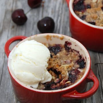 Two red mini ramekins with cherry crisp and a scoop of vanilla ice cream.