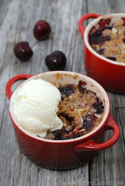 Two red mini ramekins with cherry crisp and a scoop of vanilla ice cream.