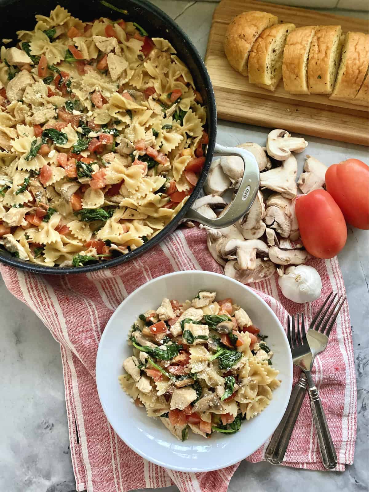 Top view of a skillet filled with pasta and a white bowl filled with the same pasta with forks.