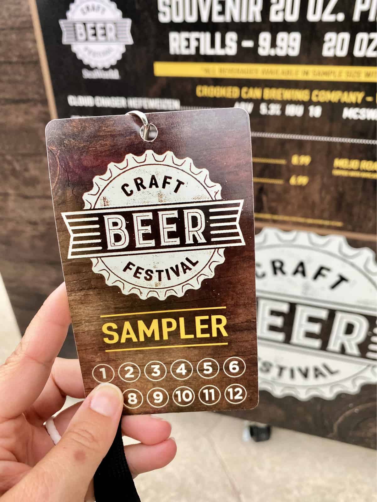 A plastic brown Craft Beer Festival Sampler lanyard held up by a hand.