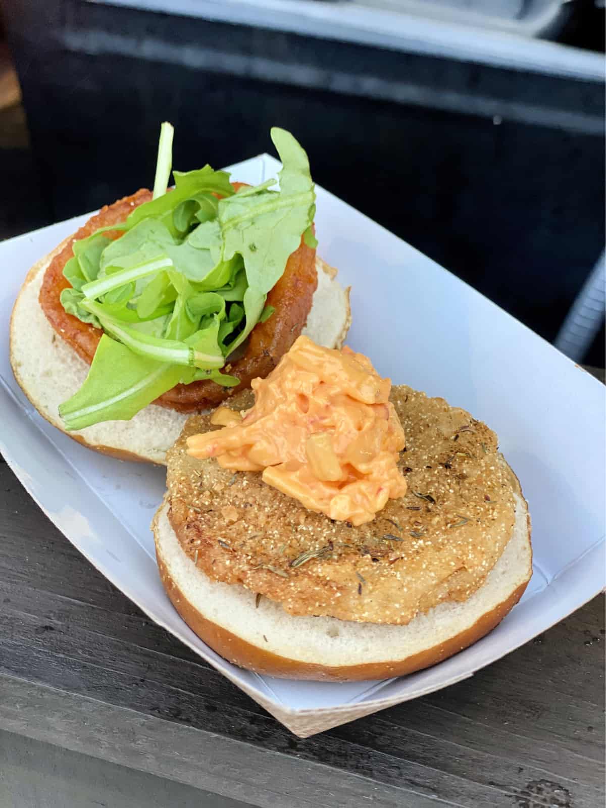Slider with fried green tomato, pimento cheese, arugula, and onion ring on a bun.