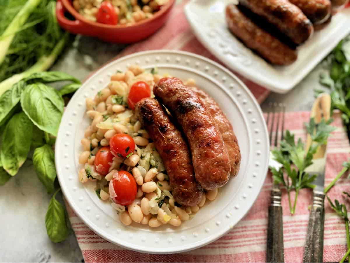 Three grilled sausage links on a bed of white beans nestled on a white plate with dots.