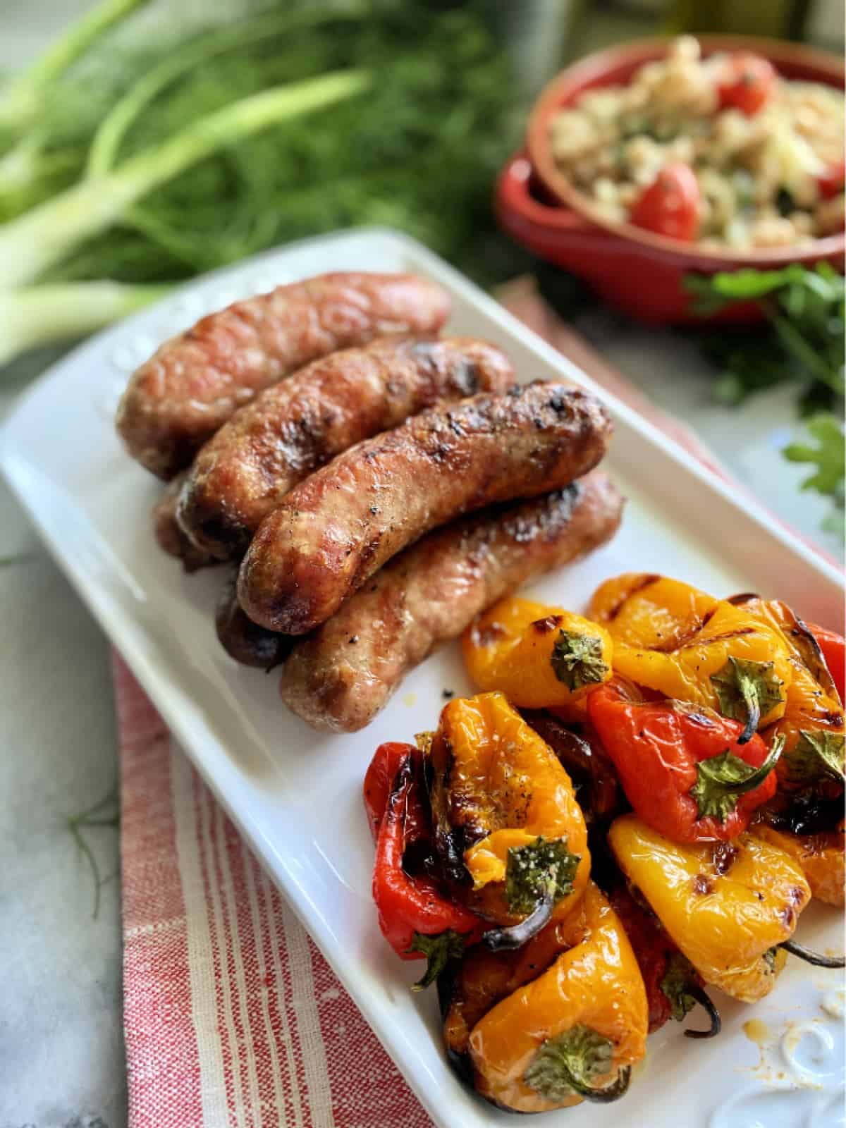 White platter resting on red and white striped cloth holding grilled sausage and bell peppers.